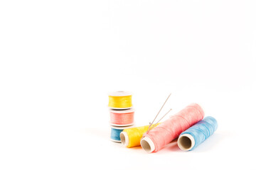 Three spools and bobbins of thread of yellow, blue and pink color with needles on a white background in a minimalistic style with a place for text. Items for needlework, embroidery and sewing.