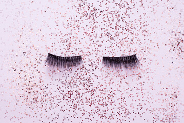False eye lashes on trendy pastel pink background with sparkles. Beauty concept. Makeup cosmetics. Top view, flat lay. Place for text - obrazy, fototapety, plakaty