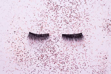 Fotobehang False eye lashes on trendy pastel pink background with sparkles. Beauty concept. Makeup cosmetics. Top view, flat lay. Place for text © Nastya