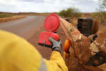 Trained competent road traffic authorize person wearing safety glove holding red warning flashing light prior placing on the damage corner of fence roadside protection  