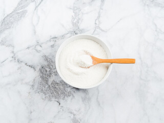 Collagen protein powder in bowl with wooden spoon on marble table. Top view