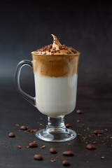 Glass of trendy fluffy creamy dalgona or whipped instant coffee with milk, coffee beans and chocolate on the dark background. New popular food and drink trend concept. Copy space.
