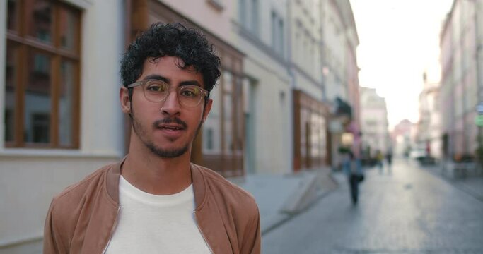 Crop view of handsome guy in glasses turning head and looking to camera. Portrait of man with nose ring smiling while standing at old city street.Concept of people and real life