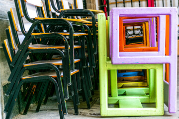 Conjunto de sillas de metal verde y madera apiladas junto con otra pila de sillas de madera de colores con formas cuadradas