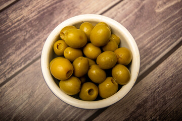 Green olives in a ceramic bowl on a wooden background . Close up.