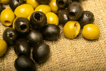 Green olives and black olives scattered on sacking with rough texture. Close up.