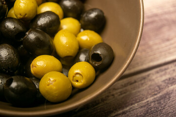 Green olives and black olives in a ceramic bowl on a wooden background. Close up.