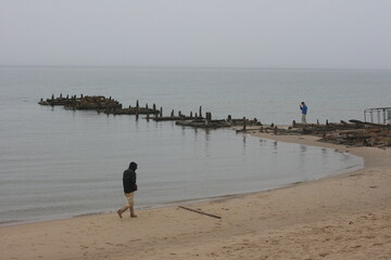 Olkhon / Russia - 27 June 2019: An old wooden pier on lake Baikal. Lonly man walk on beach on Olkhon island. Beautiful landscape with hills and lake. Copy space