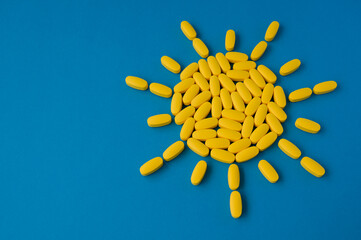 vitamin D health concept of summer yellow sun from pills tablets on blue surface with copy space