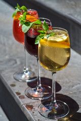 set of summer refreshments on a stone background with copy space. three glasses of red, yellow and orange lemonade.