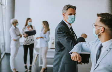 Two colleagues avoid a handshake when meeting in the office and greet with bumping elbows