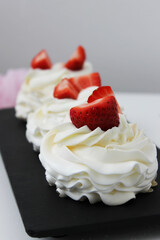Cupcakes with white cream and strawberries on a black plate. Vertical photo.