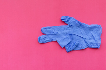 A blue medical glove on a pink background points with two fingers at an empty space for text. Selective focus.