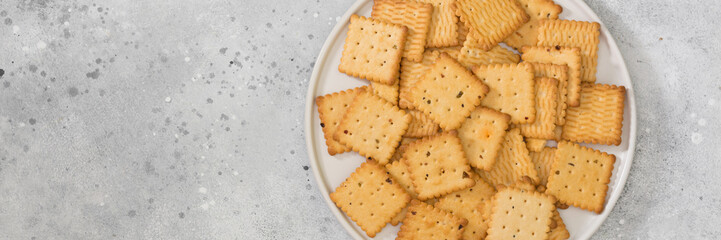 Cookies in a white plate on a light gray table. A lot of cookies in the plate. Crackers on a plate. Top view with space for text. Banner