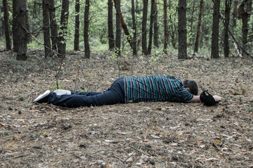 Murder in the woods. The body of a man in a blue t-shirt and trousers lies on the ground among the trees in the forest. Victim of an attack.