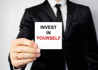 Invest in yourself, an inscription on a white piece of paper in the hand of a young businessman.