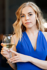 girl in blue dress standing with glass of wine.