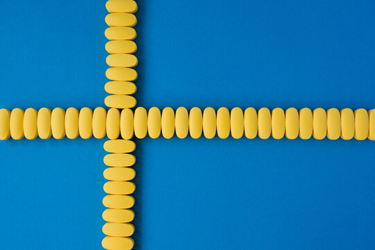 concept healthcare of yellow tablets on blue surface with copy space in form of cross on sweden flag