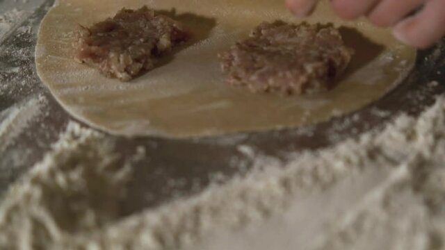 Attractive adult woman making chebureks - Georgian national dish. Process of making food, cooking at the kitchen. Raw cheburek.