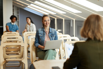 Smiling clever clogs sitting with laptop at lecture and listening to teacher at class