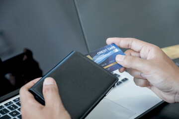 The businessman's hand is holding a credit card and using a laptop for online shopping and internet payment in the office