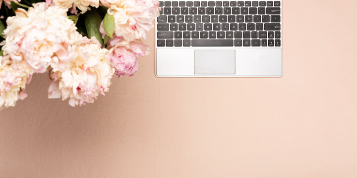 Workspace with keyboard laptop and peony flowers. Top view on a pink desk, flat lay with copy space. Office business concept