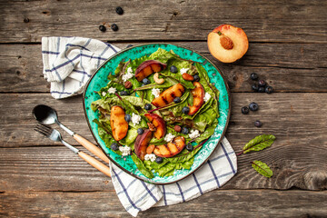 Delicious summer salad with caramelized peaches, blueberry and goat cheese, wooden background. Food recipe background. Close up