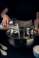 Woman in checkered apron pours milk into a bowl. Process of making bakery. Khachapuri Recipe – Georgian cheese bread.