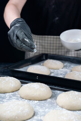 Woman in checkered apron and black gloves are sprinkling with flour a piece of yeast dough in baking tray. Process of making bakery. Adjarian Khachapuri Recipe – Georgian cheese bread.