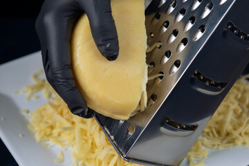 Hands in black gloves rub cheese on a grater. Home cooking. Adjarian Khachapuri Recipe – Georgian cheese bread.