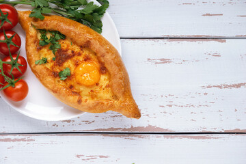 White plate with Adjarian Khachapuri – Georgian cheese bread decorated with tomatoes and parsley...
