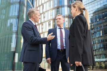 Team of business people meeting in city, standing and talking at office buildings, discussing contract. Low angle shot. Cooperation and teamwork concept