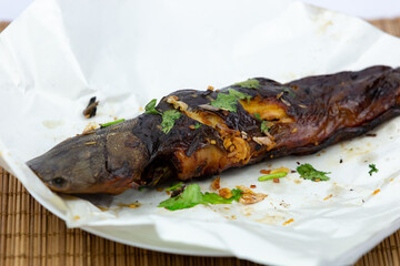Thai food, grilled fish topped with fresh Thai herbs on a bamboo tray in the studio