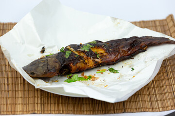 Thai food, grilled fish topped with fresh Thai herbs on a bamboo tray in the studio