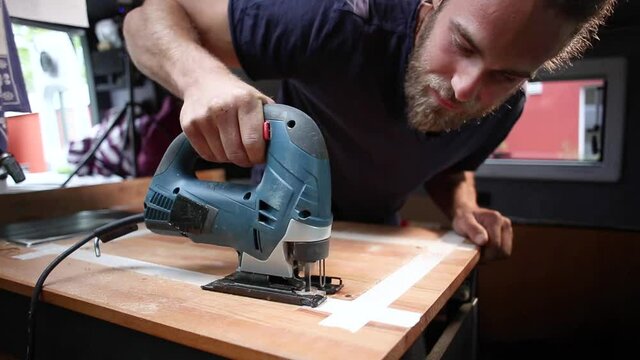 Man using a jigsaw on a wooden countertop inside a camper van