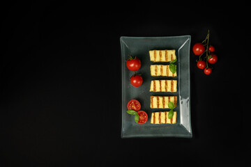 Fried slices of halloumi cheese on a plate with cherry tomatoes and Basil leaf on a dark background. Traditional cheese of Greece and Turkey. copy space. flat lay.