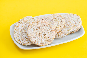 Puffed rice cakes on white dish on yellow paper background