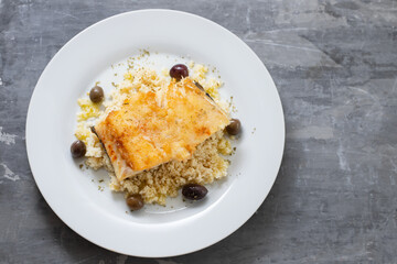 fried cod fish with cous cous and olives on white plate