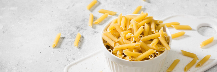 Penne pasta. Raw Penne pasta in a white bowl on a light gray table. Top view with space for text. Banner
