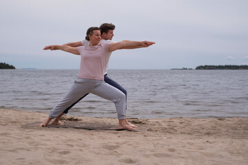 Fototapeta na wymiar fitness and healthy lifestyle concept. Man and woman making warrior pose on beach