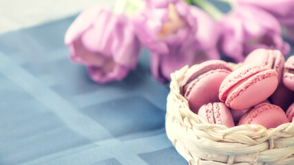 traditional French multicolored macaroons rows in a basket on the background of a bouquet of flowers. Close-up, selective focus.