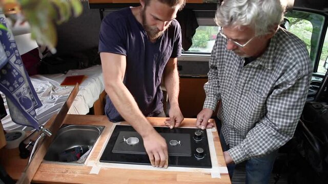 Two men installing a gas stove into a camper van