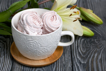 Homemade zephyr of various shapes. In a mug and on the surface of the table. Near a lily with unblown buds.