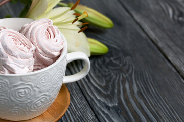 Homemade zephyr of various shapes. In a mug and on the surface of the table. Near a lily with unblown buds.