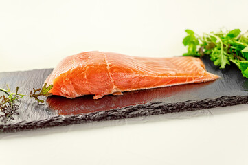 piece of smoked fresh salmon with lettuce leaves on a slate Board
