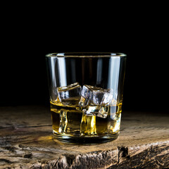 A glass of whiskey with ice cubes on a wooden table and a dark background