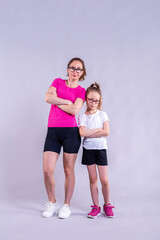 Stylish mom and daughter stand on a gray background in sportswear.