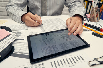 Business analysis and accounting concept - businessman working with document, spreadsheet, using calculator, tablet pc. Office desk closeup.