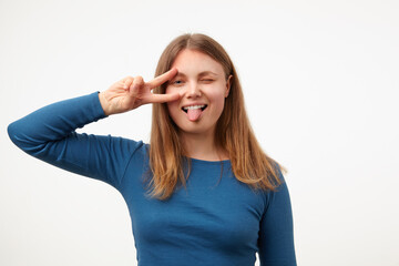 Cheerful young pretty long haired female raising hand with victory gesture to her face and showing...