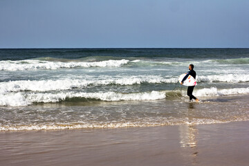 surfer, a young man with a surfboard is walking near the sea